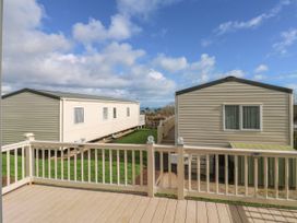 A deck with railing overlooking two mobile homes with a grassy yard and partly cloudy sky at A La Mer in Paignton