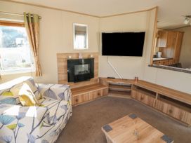 A living room with a sofa a wall mounted television and fireplace at A La Mer in Paignton