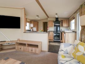 A living room with a sofa and wooden TV stand opening to a kitchen with wooden cabinets at A La Mer in Paignton