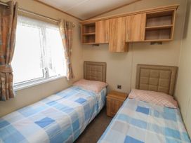 A bedroom with two single beds a window with curtains and wall cabinets at A La Mer in Paignton