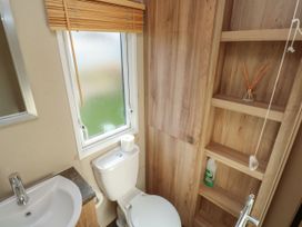 A bathroom with a toilet sink window and wooden shelves at A La Mer in Paignton