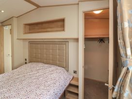 A bedroom with a bed covered by a patterned duvet a padded headboard a wooden shelf a doorway leading to a closet with hangers and a curtain tied back at A La Mer in Paignton