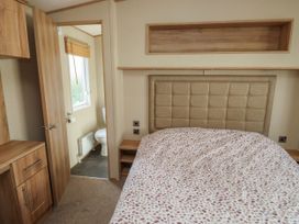 A bedroom with a bed a cushioned headboard bedside tables wooden cabinets and a partially visible bathroom at A La Mer in Paignton