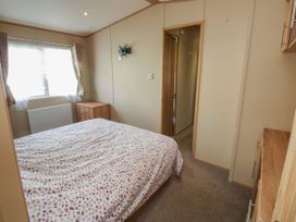 A bedroom with a bed a wooden chest of drawers a window with curtains and a door at A La Mer in Paignton