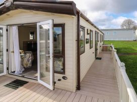 A static caravan with open glass doors leading to a deck with a railing and grass surrounding it at A La Mer in Paignton
