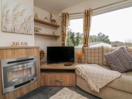 A living room with a TV on a wooden cabinet next to a sofa with cushions and a throw at Ocean View in Combe Martin