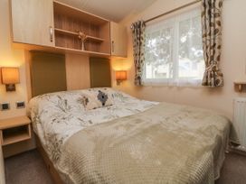 A bedroom with a bed covered with a patterned duvet and a blanket with bedside lamps and a window with curtains at Ocean View in Combe Martin