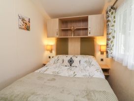 A bedroom with a bed between two wooden shelves with lamps on each side and a window with curtains at Ocean View in Combe Martin