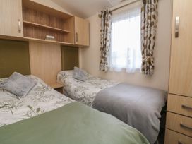 A bedroom with two single beds green and grey blankets and wooden storage units at Ocean View in Combe Martin
