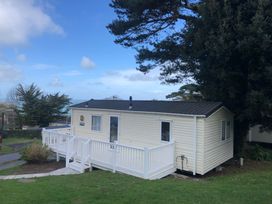 A beige mobile home with a white deck on green grass near trees and a blue sky at Ocean View in Combe Martin