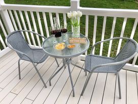 An outdoor patio table with two wine glasses red wine snacks a vase with white flowers and a sign on a deck with two gray chairs at Ocean View in Combe Martin