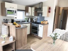 A kitchen with wooden cabinets a microwave oven a stove and a dining table with flowers at Ocean View in Combe Martin