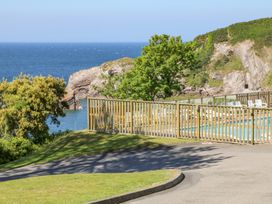 An outdoor pool area with lounge chairs and wooden fencing near a coastal cliff and the sea at Ocean View in Combe Martin