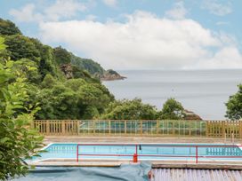An outdoor swimming pool with a red railing overlooking trees and the sea at Ocean View in Combe Martin