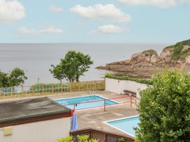 An outdoor swimming pool area with two pools near the coastline with trees rocks and the sea in the background at Ocean View in Combe Martin