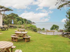 An outdoor grassy area with round wooden picnic tables and benches overlooking trees and the sea at Ocean View in Combe Martin
