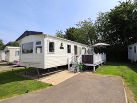 A static caravan with a deck and umbrella on a grassy lot with a bicycle in front at 25 Kingfisher Court in Tattershall