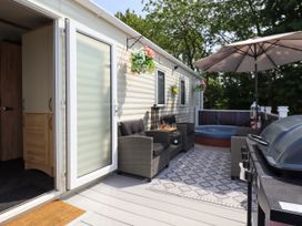 An outdoor patio area with two chairs a table a barbecue grill an umbrella and a hot tub at 25 Kingfisher Court in Tattershall