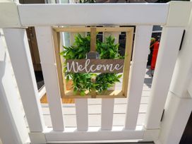 A white wooden gate with a hanging wooden welcome sign decorated with green leaves at 25 Kingfisher Court in Tattershall
