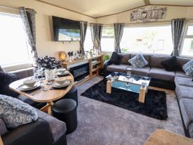 A living room with a dining table set for four a wall mounted TV a grey sectional sofa a glass coffee table and black rug at 25 Kingfisher Court in Tattershall
