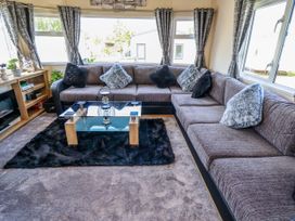 A living room with a large sectional sofa with cushions and a glass coffee table on a black rug at 25 Kingfisher Court in Tattershall
