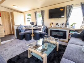 A living room with a corner dining area a glass coffee table a wall mounted television and an electric fireplace at 25 Kingfisher Court in Tattershall