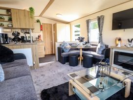A living room with a corner dining area a glass coffee table a mounted TV and a fireplace at 25 Kingfisher Court in Tattershall