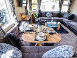 A dining area with a table set for four surrounded by a sofa with cushions in a living room at 25 Kingfisher Court in Tattershall