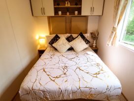 A bedroom with a bed with patterned bedding and pillows two bedside tables a lamp dried plants and wall cabinets at 25 Kingfisher Court in Tattershall