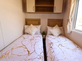 A bedroom with two single beds with patterned bedding a small plant on a bedside table and a window at 25 Kingfisher Court in Tattershall