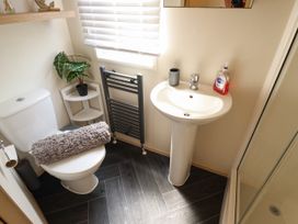 A bathroom with a toilet, a corner shelf with a plant, a sink with hand soap and a cup, a towel radiator, and a shower at 25 Kingfisher Court in Tattershall