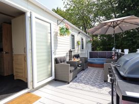 An outdoor patio with wicker chairs a hot tub an umbrella and a barbecue grill at 25 Kingfisher Court in Tattershall