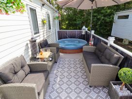 An outdoor patio with wicker sofas, a hot tub, a patterned rug, a glass table with drinks, and an umbrella at 25 Kingfisher Court in Tattershall