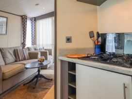 A living room with a sofa and striped cushions next to a kitchen area with a gas stove and utensils at The Boathouse in St Leonards-On-Sea