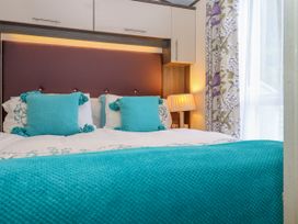 A bedroom with a bed with turquoise cushions and blanket with floral curtains and a bedside lamp at The Boathouse in St Leonards-On-Sea