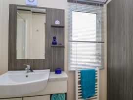 A bathroom sink with a mirror above it two small shelves a window with blinds and a towel on a radiator at The Boathouse in St Leonards-On-Sea
