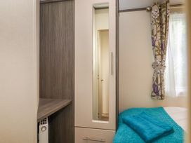 A bedroom corner with a wardrobe featuring a mirror a folded towel on a blue bedspread and floral curtains on a window at The Boathouse in St Leonards-On-Sea
