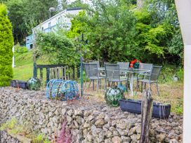 An outdoor patio area with a glass table and six metal chairs surrounded by trees and garden items at The Boathouse in St Leonards On Sea