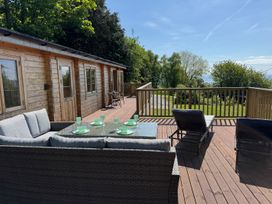 A wooden deck with outdoor seating and dining set next to a wooden cabin surrounded by trees at Northwood Lodge in Llanbedrog