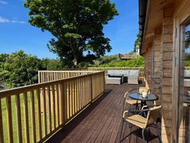 A wooden deck with outdoor seating and a table with two chairs at Northwood Lodge in Llanbedrog