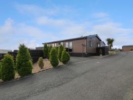 An exterior view of a single-story wooden house with shrubs and a paved driveway at 1 Fishermans Hill in Glenluce