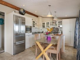 A kitchen with a glass dining table and beige chairs a stainless steel refrigerator and white cabinets at 1 Fishermans Hill in Glenluce