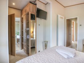 A bedroom with a bed covered with a white quilt and folded towels a wooden wardrobe with a mirror a wall-mounted television and an open door leading to a bathroom at 1 Fishermans Hill in Glenluce