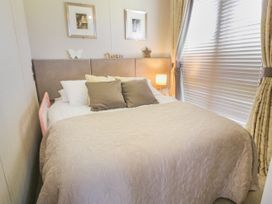 A bedroom with a bed with pillows and a quilt next to a window with blinds and curtains at 1 Fishermans Hill in Glenluce