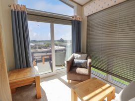 A sitting area with two wooden tables an armchair with cushions and large windows with curtains and blinds at 1 Fishermans Hill in Glenluce