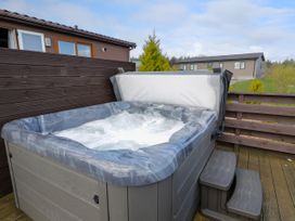 An outdoor hot tub with bubbling water on a wooden deck with a privacy fence and nearby buildings at 1 Fishermans Hill in Glenluce