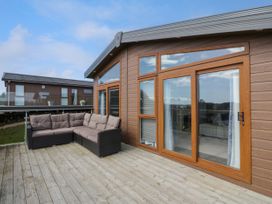 An outdoor wooden deck with a cushioned corner sofa and large wooden framed glass doors at 1 Fishermans Hill in Glenluce