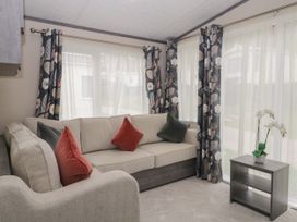 A living room with a beige corner sofa with red and green cushions floral curtains and a small wooden table with a white flower pot at Caravan 7 Plymouth