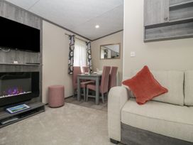 A living room with a beige sofa with a red cushion a dining table with four pink chairs a wall mounted tv and an electric fireplace at Caravan 7 in Plymouth