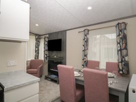 A dining area with a table set for four and a seating area with an armchair and a wall-mounted TV at Caravan 7 in Plymouth